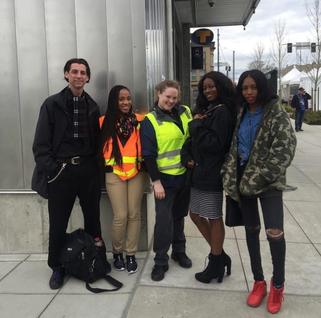 Group of five people posing outdoors, two wearing safety vests.